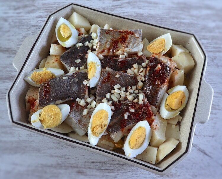 Morue aux pommes de terre, oignon, ail haché, huile d'olive, vin blanc, poivre, paprika, œufs et sel sur un plat allant au four