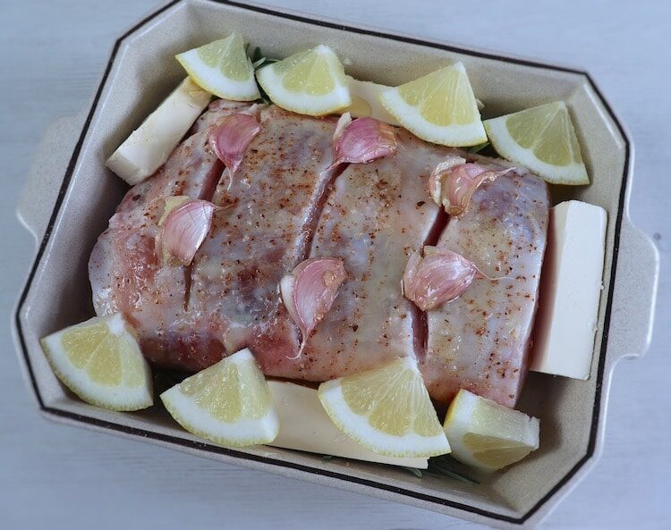 Filet de porc sur un plat allant au four avec citron, romarin, huile d'olive, margarine, ail, miel et muscade