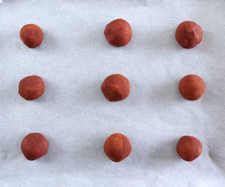 Boules de pâte au citron enrobées de poudre de cannelle sur une plaque de cuisson recouverte de papier sulfurisé